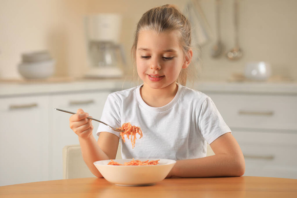 Cute little girl eating tasty pasta at table in kitchen - Foto, imagen