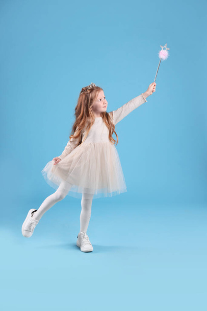 Cute girl in fairy dress with diadem and magic wand on light blue background. Little princess - Fotó, kép
