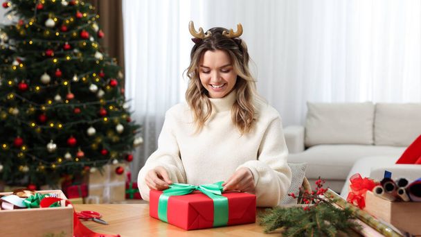 Beautiful young woman wrapping Christmas gift at home - 写真・画像