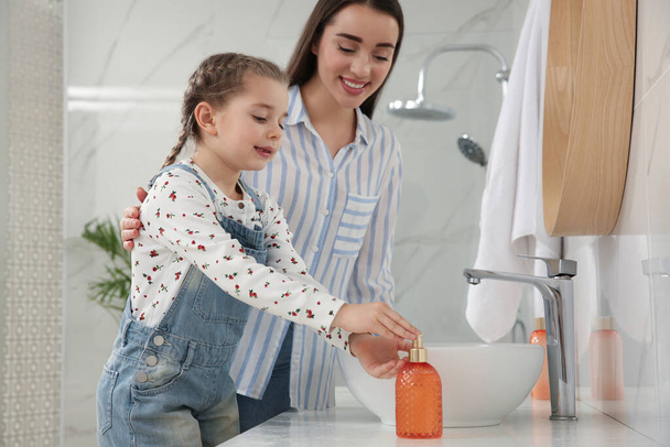 Mother and daughter washing hands with liquid soap in bathroom - Fotó, kép