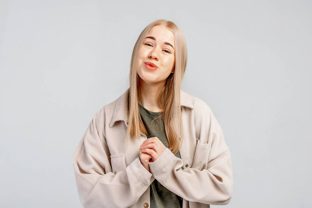 Flattered cute blonde young woman press palm chest grateful tilting head smiling, gray background. Pleased appreciating nice compliment - 写真・画像
