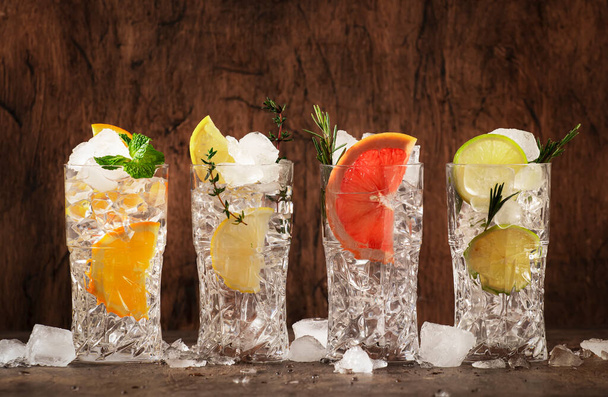 Gin tonic and citrus cocktails set. Summer drinks with lime, lemon, grapefruit, orange, soda and herbs in highball glasses, wooden counter background, cocktail party - Photo, Image