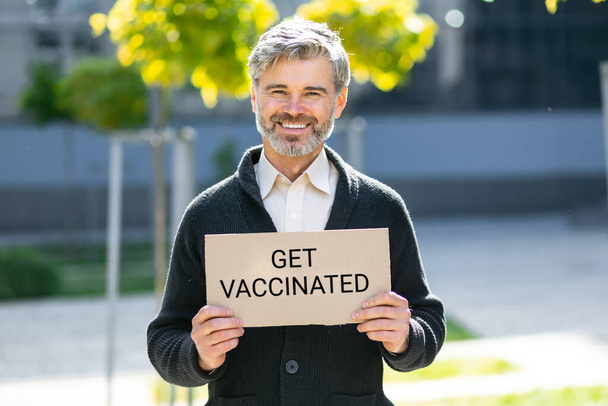 un hombre sostiene un cartel con una inscripción traducida del ucraniano vacunarse. Vacunación de apoyo humano contra el coronavirus, la gripe y otras enfermedades - Foto, Imagen