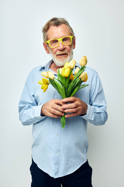 Retrato de homem sênior feliz um buquê de flores com óculos como fundo de luz do presente - Foto, Imagem