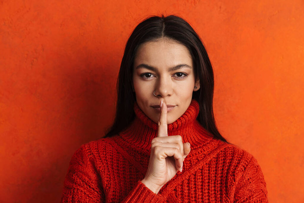 Young hispanic woman looking at camera and showing silence gesture isolated over orange wall - Foto, Imagem