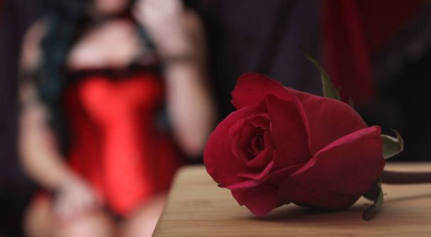 Červená růže se ženou v červeném korzetu na pozadí - Fotografie, Obrázek