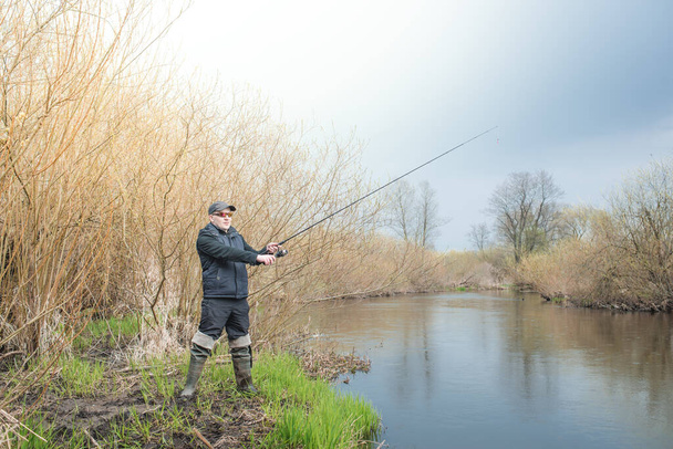 Fisherman pulls a fish with a spinning rod standing on the river. Male hobby. - Foto, afbeelding