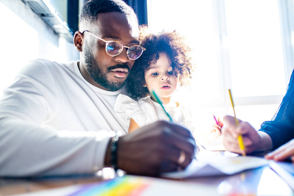 father wearing glasses and adorable little daughter drawing colorful pencils spending leisure time on weekend together - Foto, afbeelding