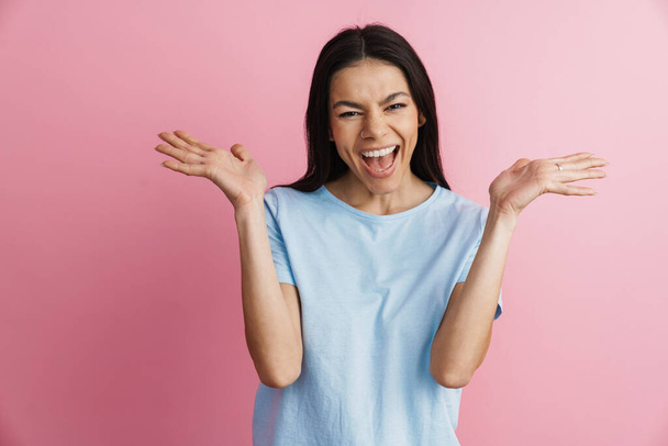 Excited hispanic woman holding copyspace and screaming at camera isolated over pink wall - Foto, afbeelding