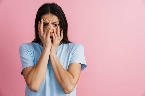 Young hispanic scared woman covering her face and looking at camera isolated over pink wall - Photo, Image