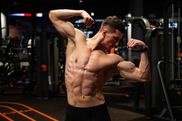 Strong guy with fit torso flexing arms muscles standing in double biceps pose in gym, strength - Foto, Bild