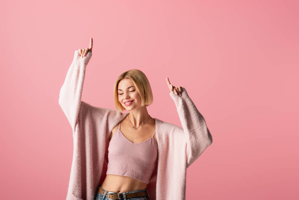 happy young woman in soft cardigan pointing with fingers isolated on pink  - Foto, Imagem