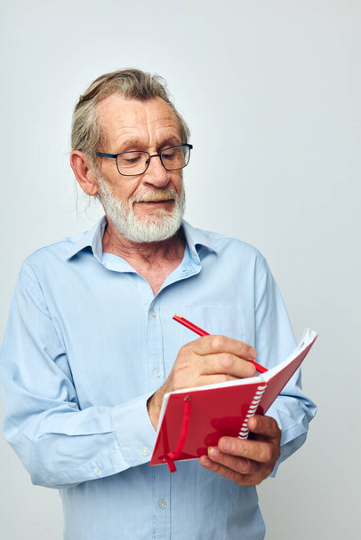 Senior grey-haired man with red notebook and pen light background - Photo, image