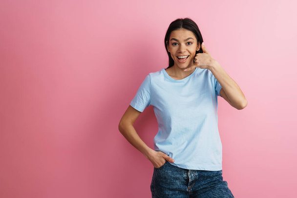 Brunette hispanic woman smiling and making handset gesture isolated over pink wall - Фото, зображення
