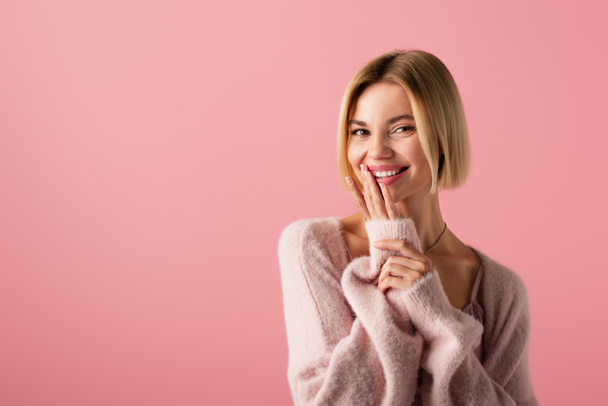 glückliche junge Frau in weicher Strickjacke, die die Lippen auf rosa isoliert berührt  - Foto, Bild