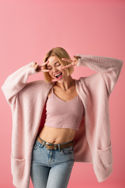 happy young woman in soft cardigan showing peace isolated on pink  - Фото, зображення