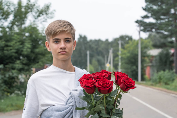 Bello adolescente tiene in mano un mazzo di rose rosse.  - Foto, immagini
