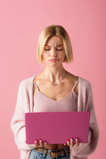 displeased young woman using laptop isolated on pink  - Foto, Imagen