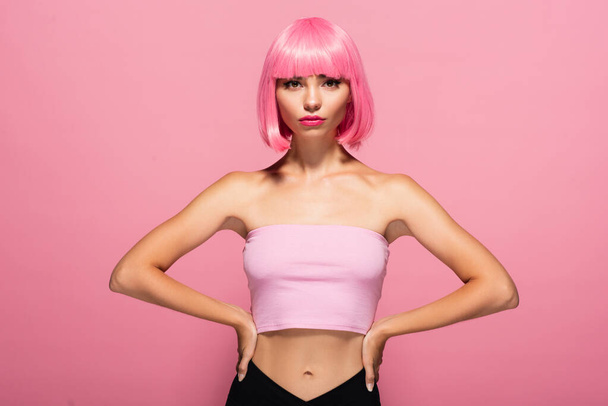 young woman with bangs and colored hair posing with hands on hips isolated on pink  - 写真・画像