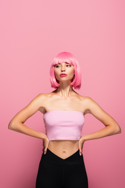 young model with bangs and colored hair posing with hands on hips isolated on pink - 写真・画像