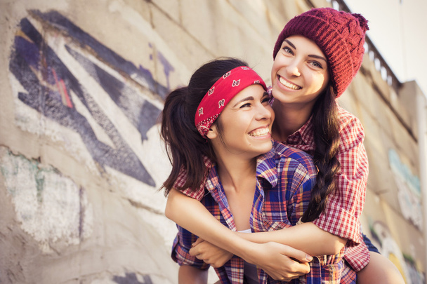 Two Brunette teenage girls friends in hipster outfit (jeans shorts, keds, plaid shirt, hat) with a skateboard at the park outdoors. Copy space - Foto, Imagem
