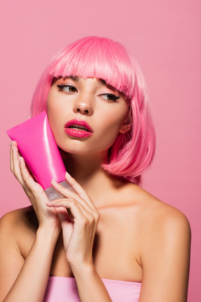 young woman with colored hair holding tube with lotion isolated on pink  - Foto, Imagem