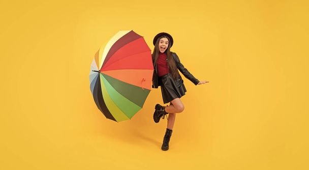 menina adolescente feliz em chapéu e roupas de couro se divertindo com guarda-chuva arco-íris, diversão de outono - Foto, Imagem
