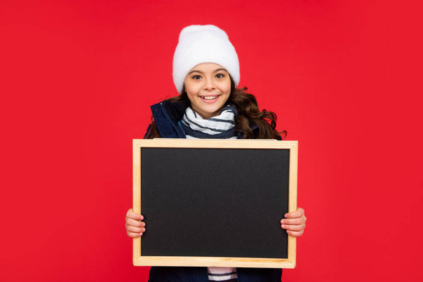 glad kid with blackboard in hat. teen girl holding chalkboard with copy space. child back to school. - Fotó, kép