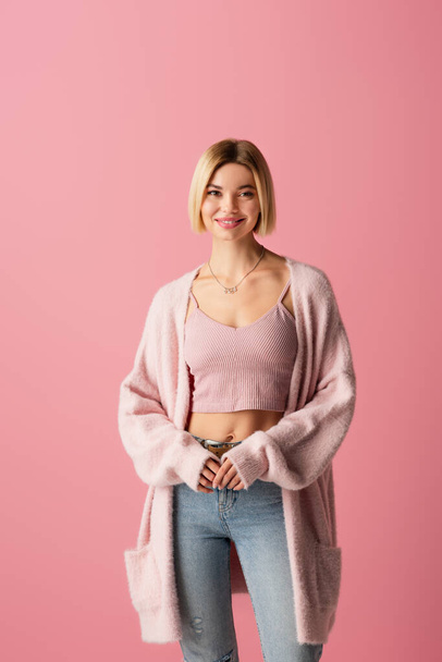 young and happy woman in soft cardigan isolated on pink  - Fotó, kép