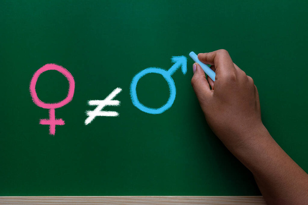 Концепция гендерного неравенства опирается на доску. Рука вычеркивает знак равенства, символ женщины и мужчины - Фото, изображение