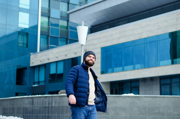Urban portrait of young elegant business man in winter casual clothes, jacket, hat. Walking in the city street, talking on the phone, making selfie. Working outdoor. - Valokuva, kuva