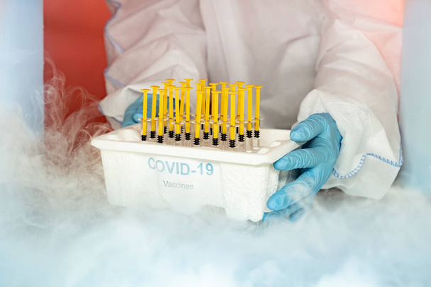 Lékařský personál s modrými rukavicemi a ochranným vybavením vyjímající krabici očkovacích látek ve skladu mrazáku prostoru covid-19 nemocnice - Fotografie, Obrázek