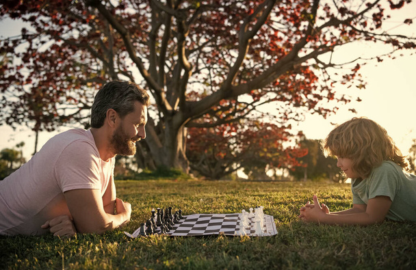 père et fils jouant aux échecs sur l'herbe dans le parc. la fête des pères. famille heureuse. parentalité et enfance. - Photo, image