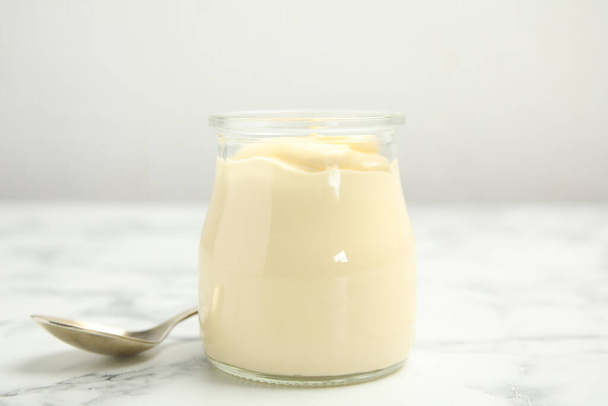Jar of delicious mayonnaise and spoon on white marble table - Фото, изображение