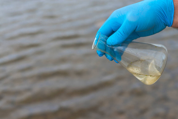 Sample water from the river for analysis. Hand in glove holding a test tube.ecology concept - Foto, Bild