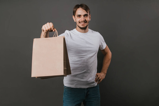 A man in a white t-shirt with a paper bag in his hands on a gray background.Mock-up - Фото, зображення