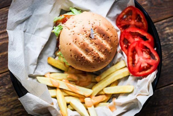 Hamburger fatti in casa serviti con patatine fritte e pomodori su un tavolo di legno. Fast food e cibo spazzatura. - Foto, immagini