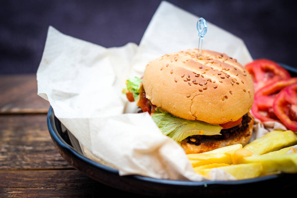 Hausgemachte Hamburger serviert mit Pommes und Tomaten auf einem Holztisch. Fast Food und Junk Food. - Foto, Bild