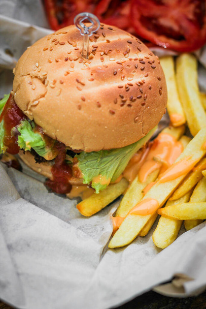 Hambúrgueres caseiros servidos com batatas fritas e tomates em uma mesa de madeira. Fast food e junk food. - Foto, Imagem