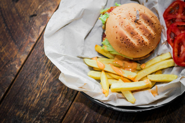 Hausgemachte Hamburger serviert mit Pommes und Tomaten auf einem Holztisch. Fast Food und Junk Food. - Foto, Bild
