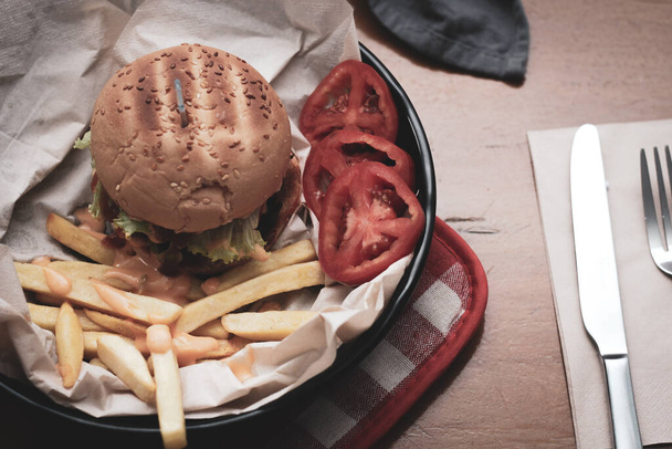 Hamburger fatti in casa serviti con patatine fritte e pomodori su un tavolo di legno. Fast food e cibo spazzatura. Con tono moderno - Foto, immagini
