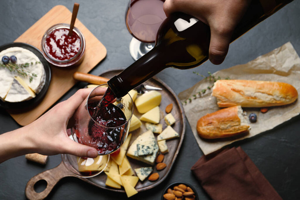Man pouring red wine from bottle into glass over black table with snacks, top view - Photo, image