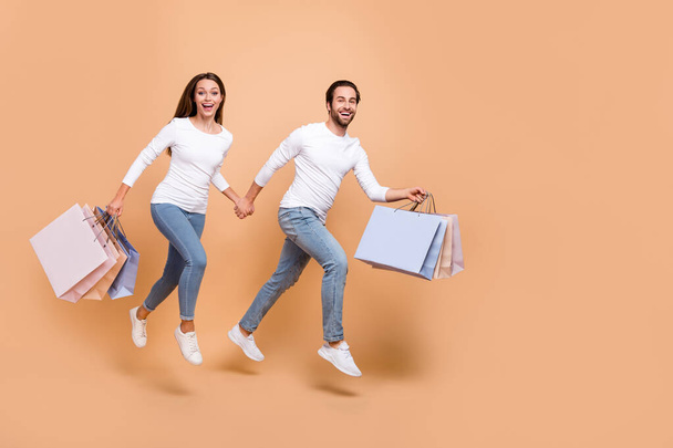 Full length body size view of beautiful handsome trendy friends friendship jumping carry bags isolated over beige pastel color background - 写真・画像