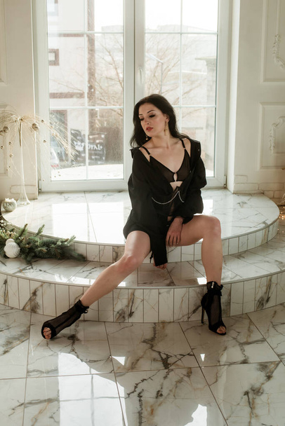 A young attractive girl in high heels a dancer with dark hair in a black shirt and a corset with chains is dancing near a large stained glass window on a marble floor  - Foto, Bild