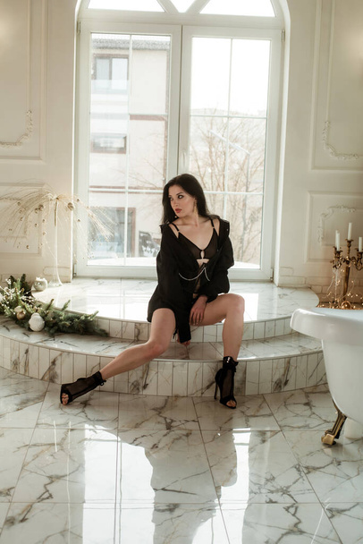 A young attractive girl in high heels a dancer with dark hair in a black shirt and a corset with chains is dancing near a large stained glass window on a marble floor  - Fotó, kép