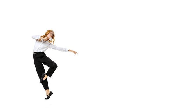 Full-length portrait of young blonde girl in white shirt and black trousers moves isolated on white background. Finance, ballet, art, business, beauty concept. - Фото, изображение