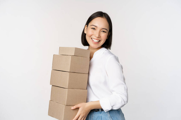 Nuoren aasialaisen naisen muotokuva, jolla on laatikoita, kuljettaa tavaraa. Korealainen naisyrittäjä koota järjestys, pysyvän voer valkoinen tausta - Valokuva, kuva