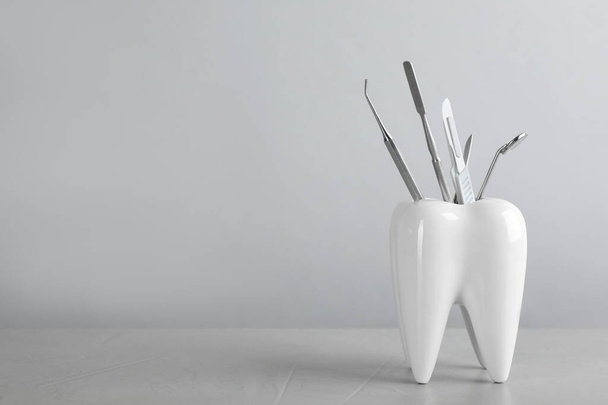 Tooth shaped holder with dentist's tools on light grey table. Space for text - Foto, immagini