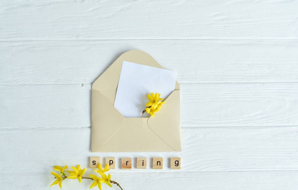Witam wiosnę. Drewniane litery SPRING i żółte kwiaty wewnątrz koperty na białym tle. Międzynarodowy Dzień Kobiet. - Zdjęcie, obraz