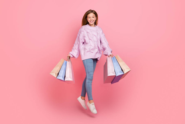 Photo of sweet charming girl dressed knitted pullover jumping high holding shoppers isolated pink color background - Foto, Imagen